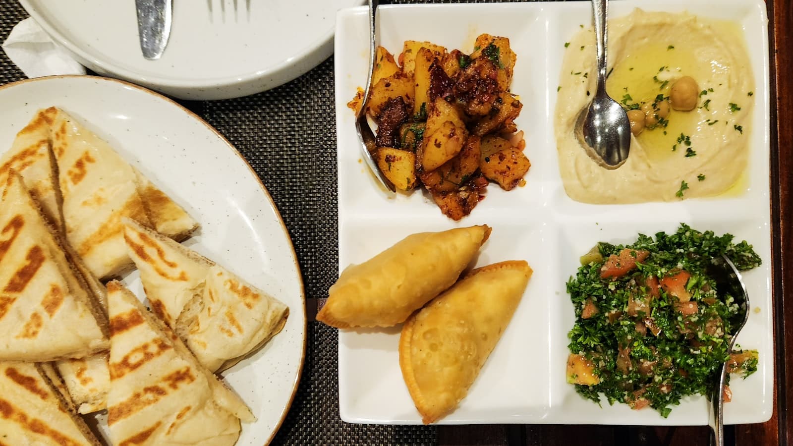Editorial top-down photograph of a Lebanese mezze platter on dark walnut wood, with hummus, baba ganoush, tabbouleh, and grilled flatbread.