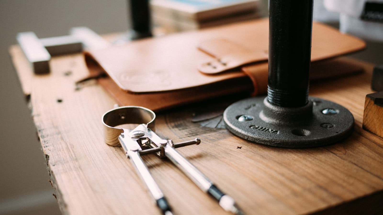 Editorial top-down photograph of a workshop bench with vintage brass calipers, a leather-bound sketchbook, a drafting compass, and a precision wrench on weathered oak wood.