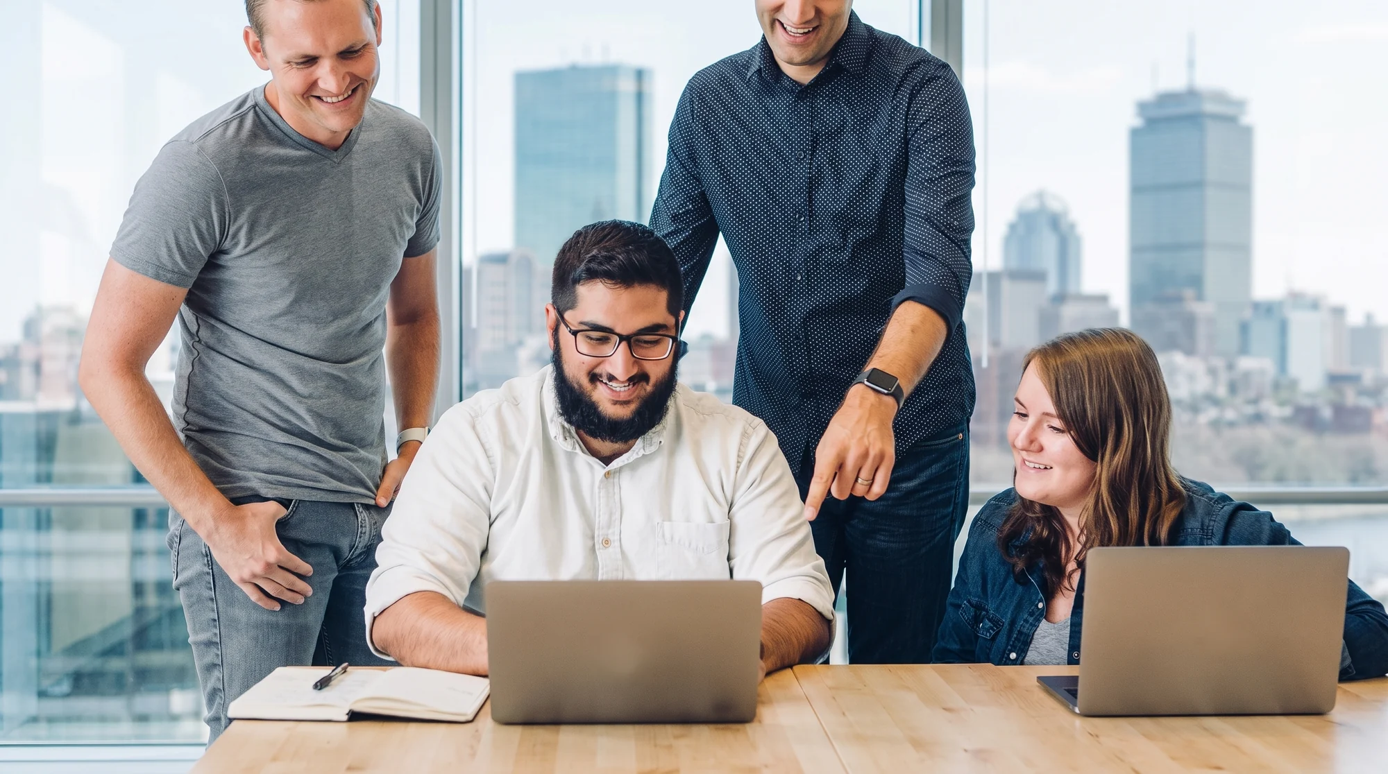 A team laughing together around a laptop in a Boston office